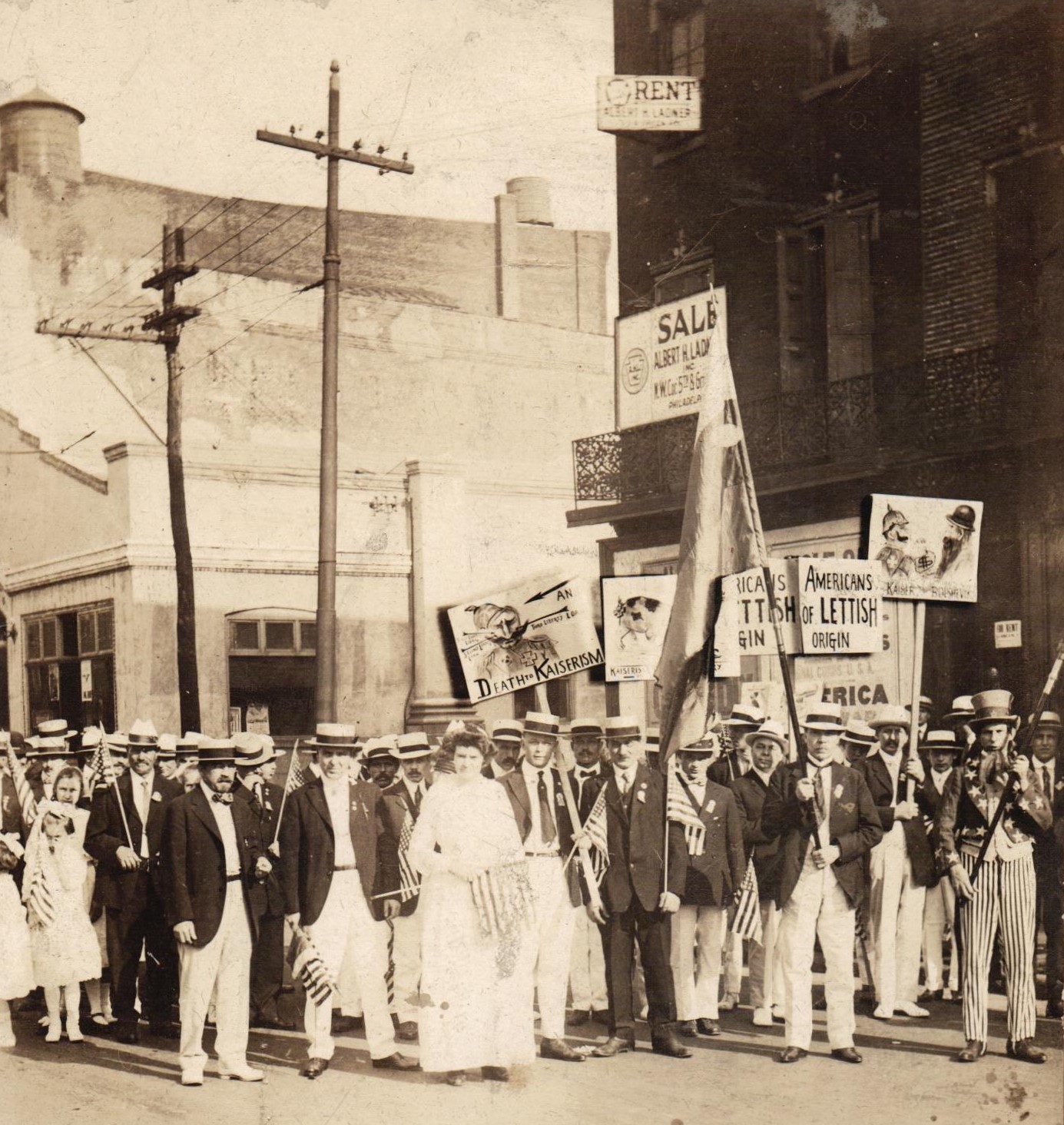 Latviešu grupa Filadelfijas ielās ar Latvijas karogu zili–zaļi–zeltītās krāsās Amerikas Savienoto Valstu Neatkarības dienas parādē 1918.gada 4.jūlijā. Politisko plakātu autors mākslinieks Georgs Āboltiņš.